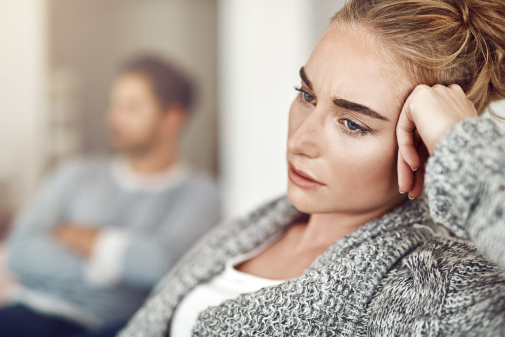 Woman Sitting With Head In Hand Looking Sad With Man In The Background Appearing Anxious